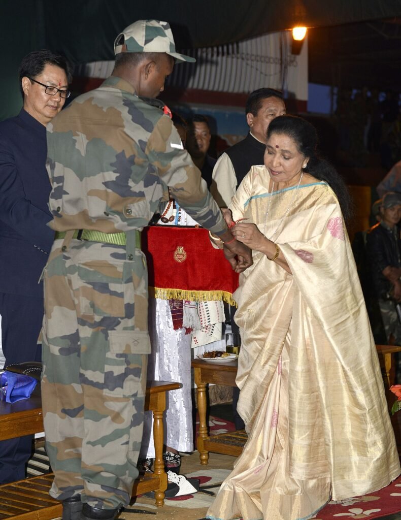 Legendary singer Ms. Asha Bhosle tying ‘Rakhi’ to a Jawan, at Bomdila, Arunachal Pradesh on August 18, 2016. The Minister of State for Home Affairs, Shri Kiren Rijiju is also seen.jpg — related to The Songs Nobody Else Wanted